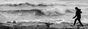 Künstlerische Schwarzweiss Fotografie. Eine Person geht über Fesen am Strand der Adria. Hohe Wellen kommen vom Meer.